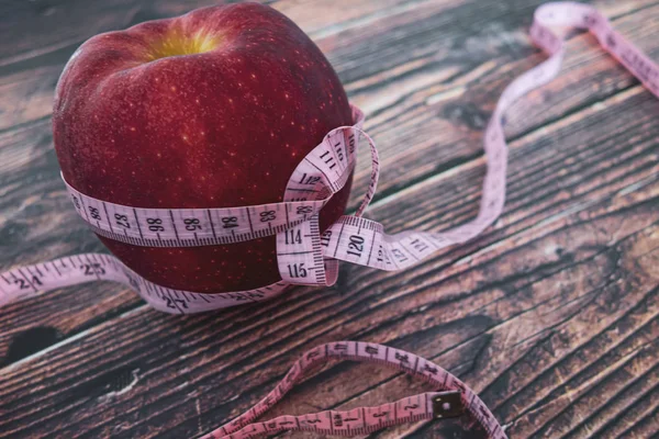 Weight loss and diet. Big juicy red apple and a tape for measuring the body. Proper nutrition and fitness. Flat lay on a wooden table. Macro