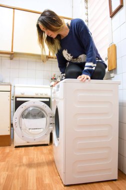 Mutfakta çamaşır makinesinde oturan kadın..