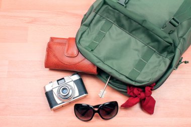 Ahşap yüzey üzerinde şık aksesuarlarla dolu sırt çantasının yakın plan fotoğrafı.