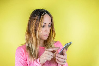 Sarıya izole edilmiş akıllı telefon kullanan güzel bir genç kadının portresi.