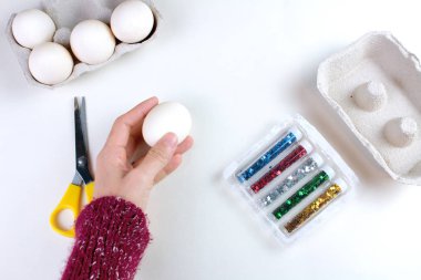 Genç kadının Paskalya yumurtaları holding beyaz masaya makas ve glitter kırpılmış görünümü