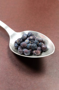 Kahverengi arka plan üzerinde gümüş kaşık ardıç Tohumu