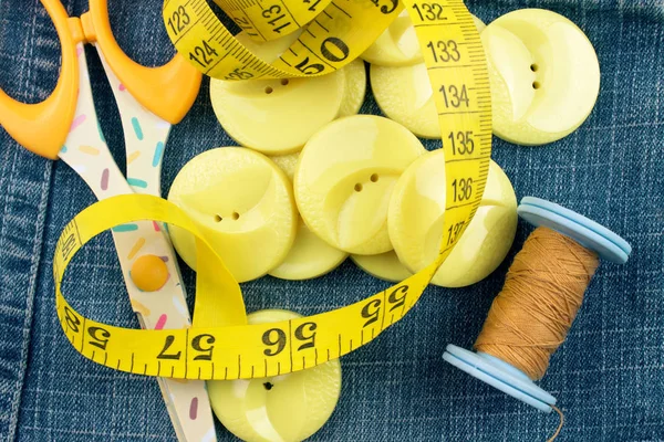 top view of yellow buttons, threads, scissors and measuring tape on jeans background