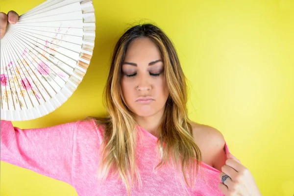 portrait of beautiful young woman with fan isolated on yellow