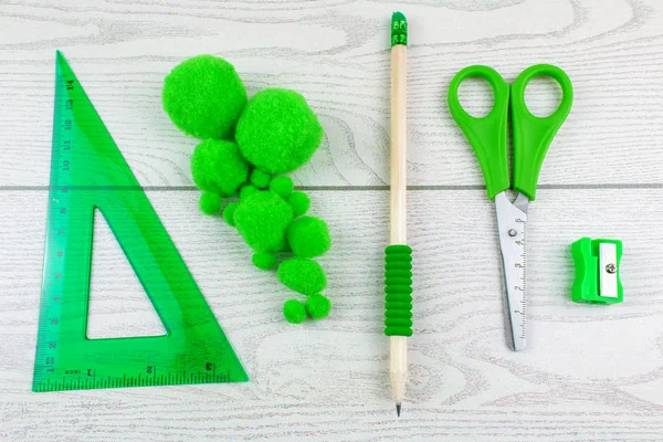 top view of green felt balls, sharpener, pencil, scissors, and ruler on white wooden background