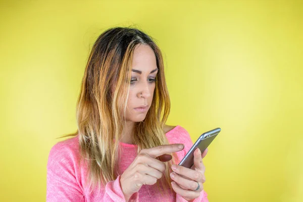 Sarıya izole edilmiş akıllı telefon kullanan güzel bir genç kadının portresi.