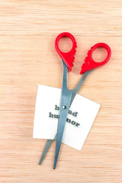 Red scissor cutting bad humor note on wooden table