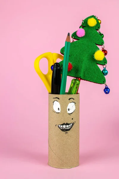 Empty Roll of Bathroom Paper with Funny Face, scissors, pens, pencils and christmas tree isolated on pink