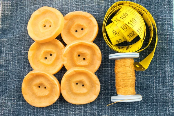 top view of yellow buttons, threads and measuring tape on jeans background