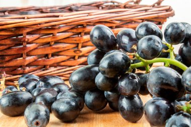 Ahşap masa üzerinde mavi üzüm demet yakınındaki hasır sepet