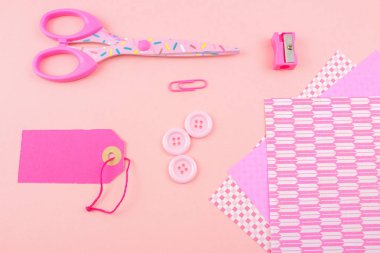 pembe makas, kalem, düğmeler, kalemtıraş, etiket ve pembe kağıtlara 