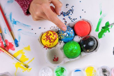 Genç kadının boyalı Paskalya yumurta beyaz masaya ışıltılı kırpılmış görünümü