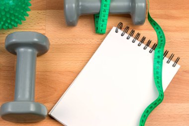 halterler, boş not defteri ve ahşap arka plan üzerinde ölçüm bandı