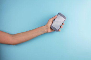 Mavi arka planda akıllı telefonu tutan bir kadının kırpılmış görüntüsü.