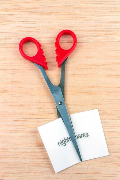Red scissor cutting nightmares note on wooden table
