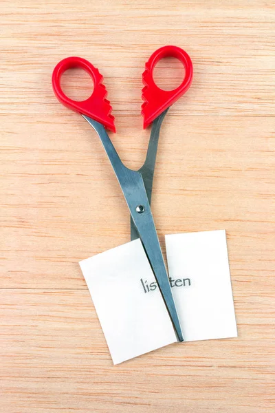 Red scissor cutting listen note on wooden table