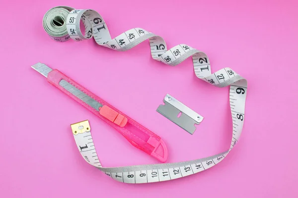 Pink Plastic Cutter, blade and measuring tape on Paper background