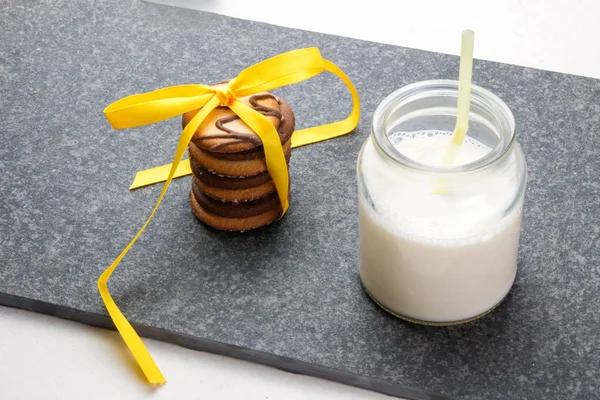 甘いクッキーと素朴なダークウッドのテーブルにリボンとガラスの瓶でミルク — ストック写真