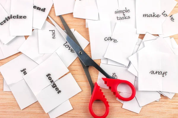 red scissors and cutted paper with words on wooden Background