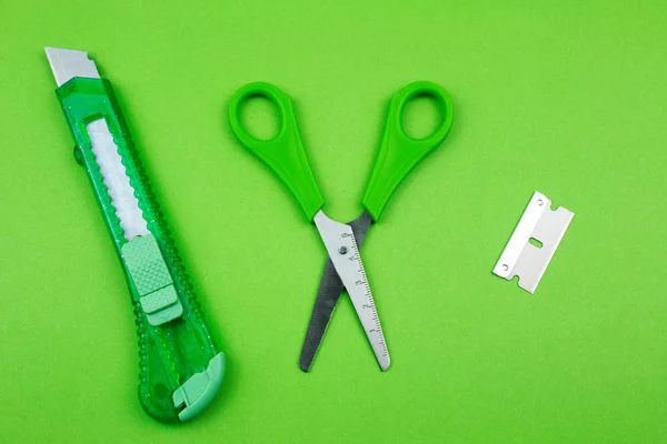 Green Plastic Cutter, blade and scissors on Paper background