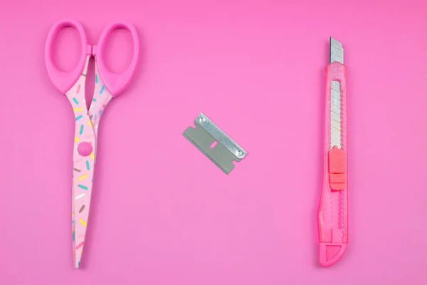 Pink Plastic Cutter, blade and scissors on Paper background