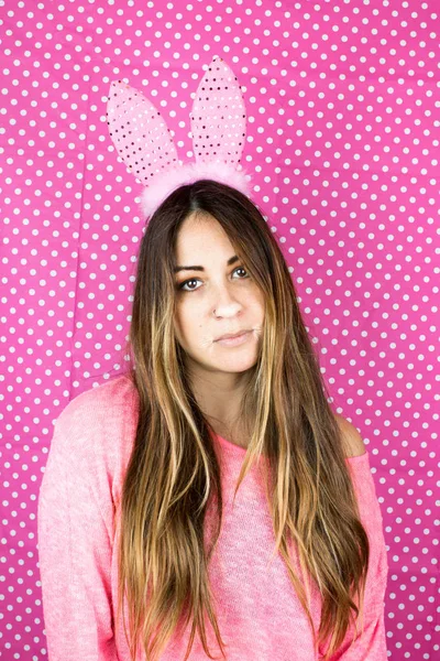 portrait of beautiful young woman with bunny ears on dotted pink background