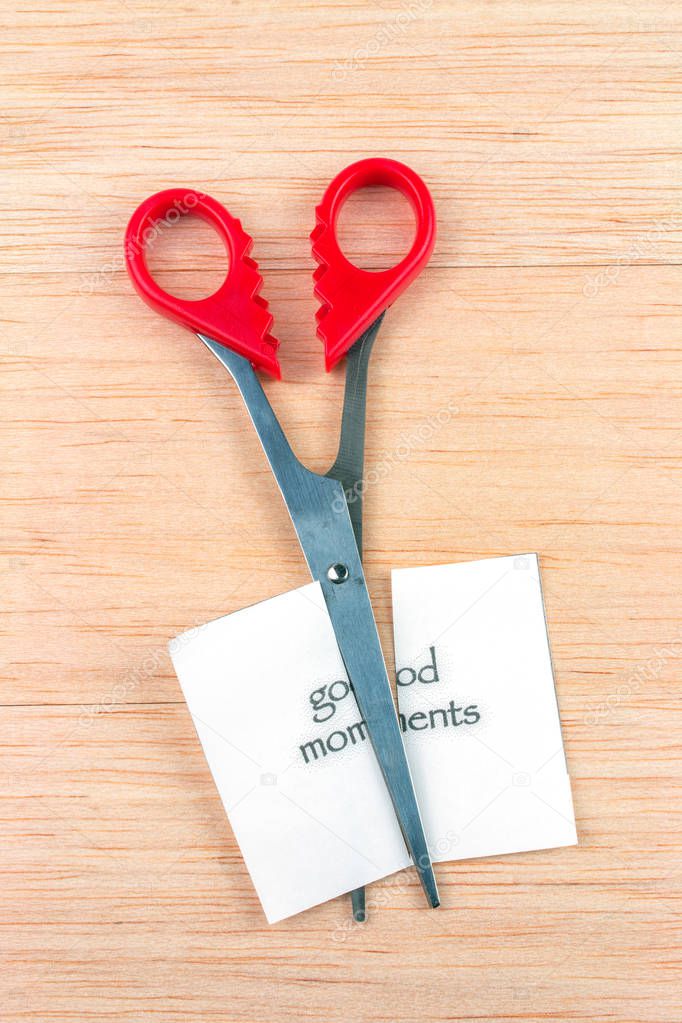 Red scissor cutting good moments note on wooden table