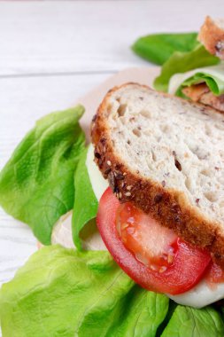Beyaz ahşap masada ekmek, peynir, domates ve salata ile sandviç 