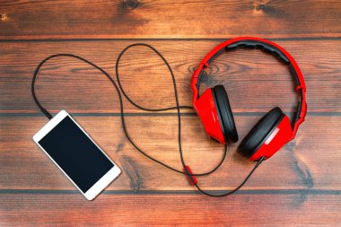 Yakın plan akıllı telefon ve kulaklıkları ahşap masa üstünde.