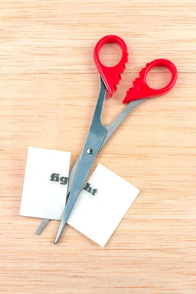 Red scissor cutting fight note on wooden table