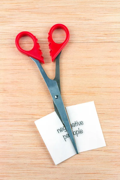 Red scissor cutting negative people note on wooden table