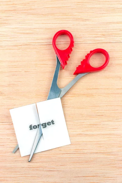Red scissor cutting forget note on wooden table