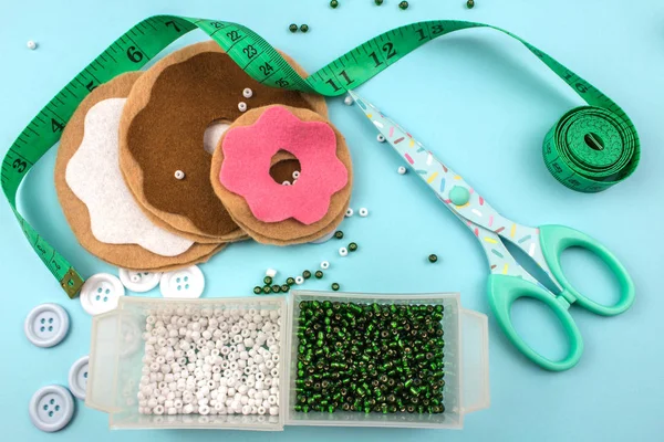 makas, boncuklar, düğmeler ve mavi arka plan üzerinde ölçüm bandı ile keçe çörek