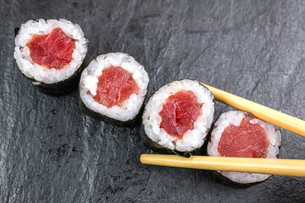 top view of sushi rolls with tuna on black stone table with chopsticks