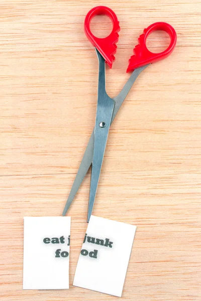 Red scissor cutting eat junk food note on wooden table