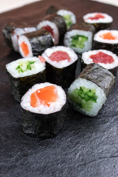 sushi rolls with tuna, cucumber and salmon on black stone table with copy space