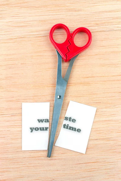 Red scissor cutting waste your time note on wooden table