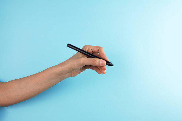 cropped shot of female hand holding pen on blue background
