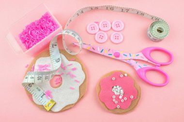 makas, boncuklar, düğmeler ve pembe bir arka plan üzerinde ölçüm bandı ile keçe çörek