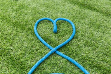 Mavi ip yeşil çimlerin üzerinde bir kalp oluşturuyor.