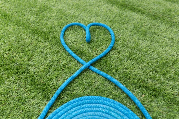 Mavi ip yeşil çimlerin üzerinde bir kalp oluşturuyor.