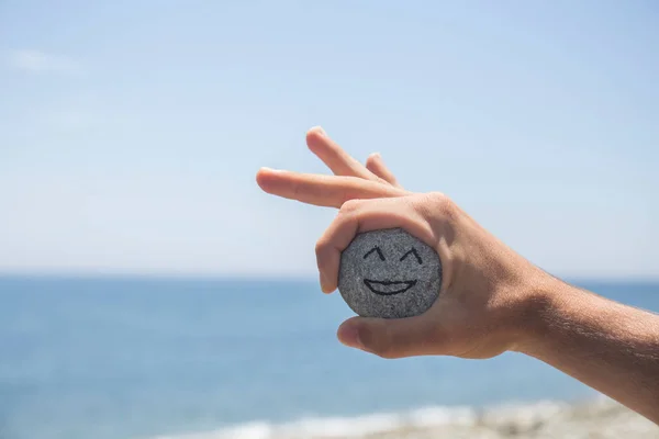 Hand Håller Sten Med Målad Glad Ansikte Bakgrunden Kan Havet — Stockfoto