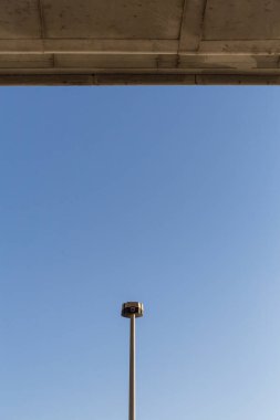 Bir sokak lambasının tepesine yakın çekim, açık mavi gökyüzü.