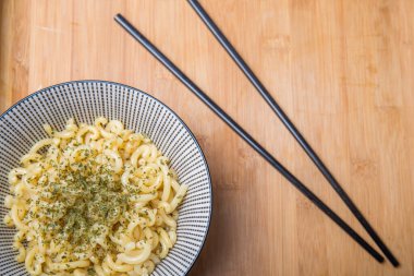 Baharatlı makarna dolu siyah beyaz seramik kâse ve yanında da ahşap masa manzarası olan çubuklar.