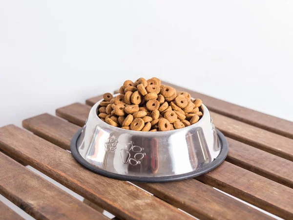 Gümüş kase köpek mamasıyla dolu tahta bir masa ve beyaz arka plan