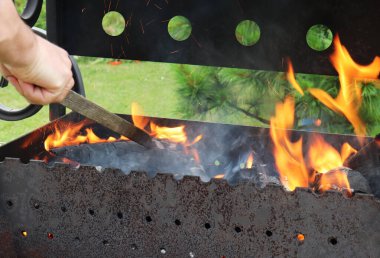 Bir adam açık havada mangal yaparken ateş yakar.