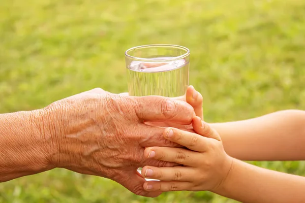 Grootmoeder die een glas schoon water aan een kind geeft. Selectieve focus. — Stockfoto
