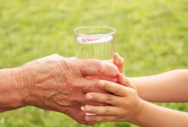 Grootmoeder die een glas schoon water aan een kind geeft. Selectieve focus. — Stockfoto