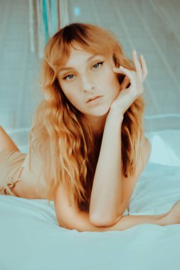 Beyaz perdeli, bungalovda yatan çekici kızıl saçlı manken. Genç seksi modelin portreleri mükemmel vücutta..