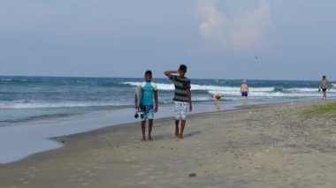 Sri Lanka 'daki Arugam Körfezi Sahili' nden geçen bir turist ve sörf tahtasıyla yürüyen çocuklar.
